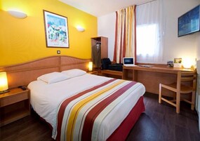 A hotel room with a bed, desk, chair, and a painting on the wall.