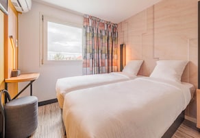 Una habitación de hotel con dos camas, un escritorio, una silla y un ventanal con cortinas.