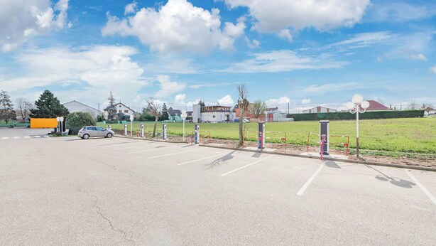 A parking lot with multiple parking spaces, a car, and a building in the background. - Hotel Roi Soleil Sausheim (Sausheim)