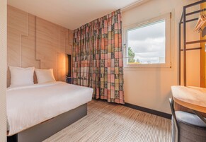 Habitación de hotel con cama, ventana, silla y cortina de estampado geométrico.