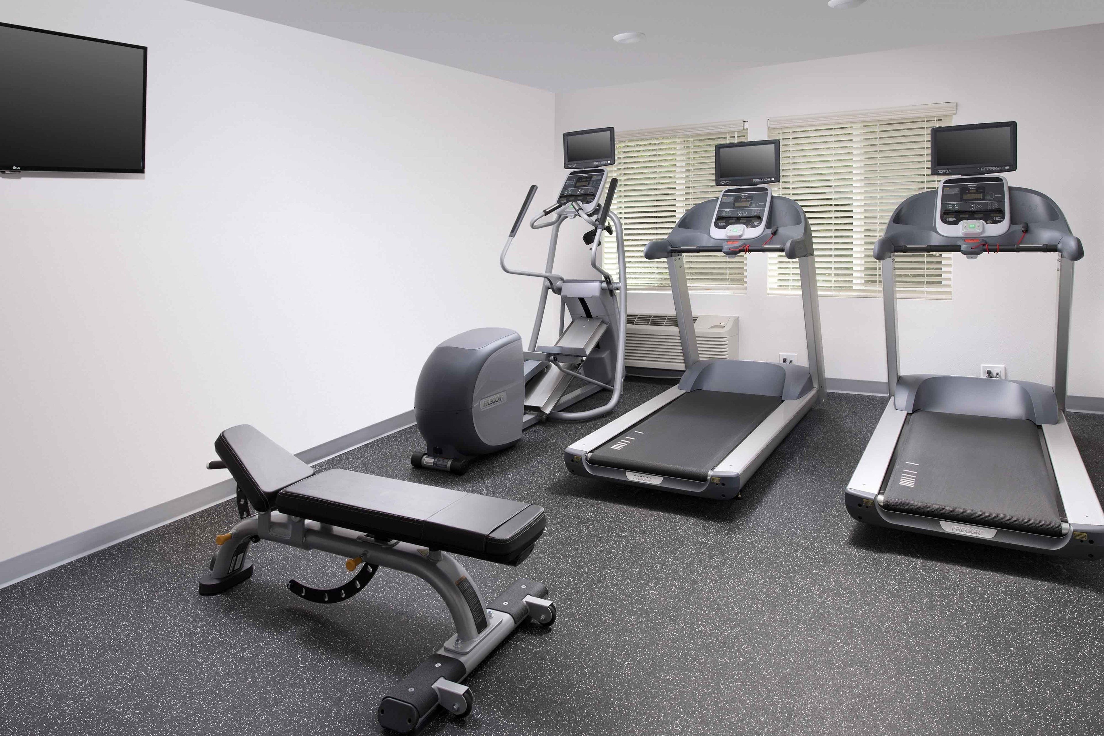 Un gimnasio con cintas de correr, elíptica y banco.
