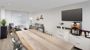 A modern kitchen with a wooden dining table, white chairs, a coffee machine, and a flat-screen TV. - WoodSpring Suites Seattle Redmond (Redmond)