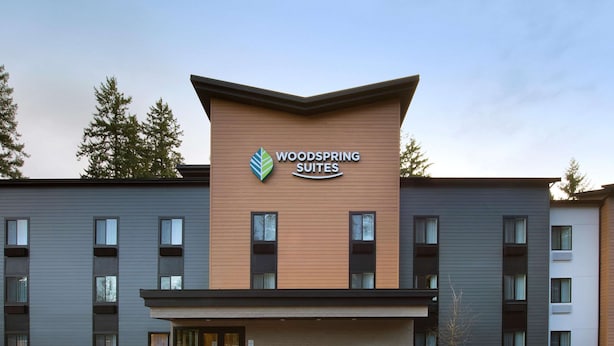 A modern hotel building with a prominent sign for "Woodspring Suites". - WoodSpring Suites Seattle Redmond (Redmond)
