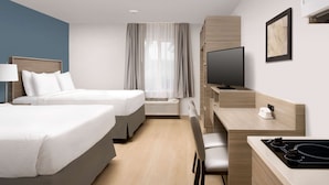A hotel room with two beds, a desk with a TV, a microwave, and a small seating area. - WoodSpring Suites Seattle Redmond (Redmond)