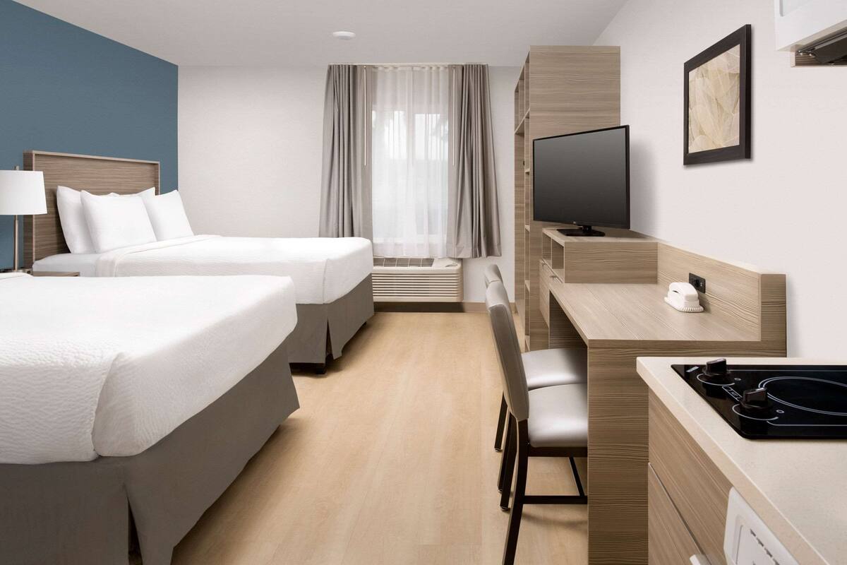A hotel room with two beds, a desk with a TV, a microwave, and a small seating area.