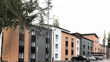 Un edificio moderno con varios pisos, espacios de estacionamiento y algunos vehículos estacionados al frente.