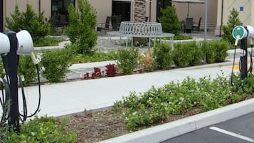 Electric vehicle charging stations in a landscaped area with outdoor seating and a building in the background.