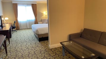 A hotel room with a bed, a sofa, a desk, and a lamp.