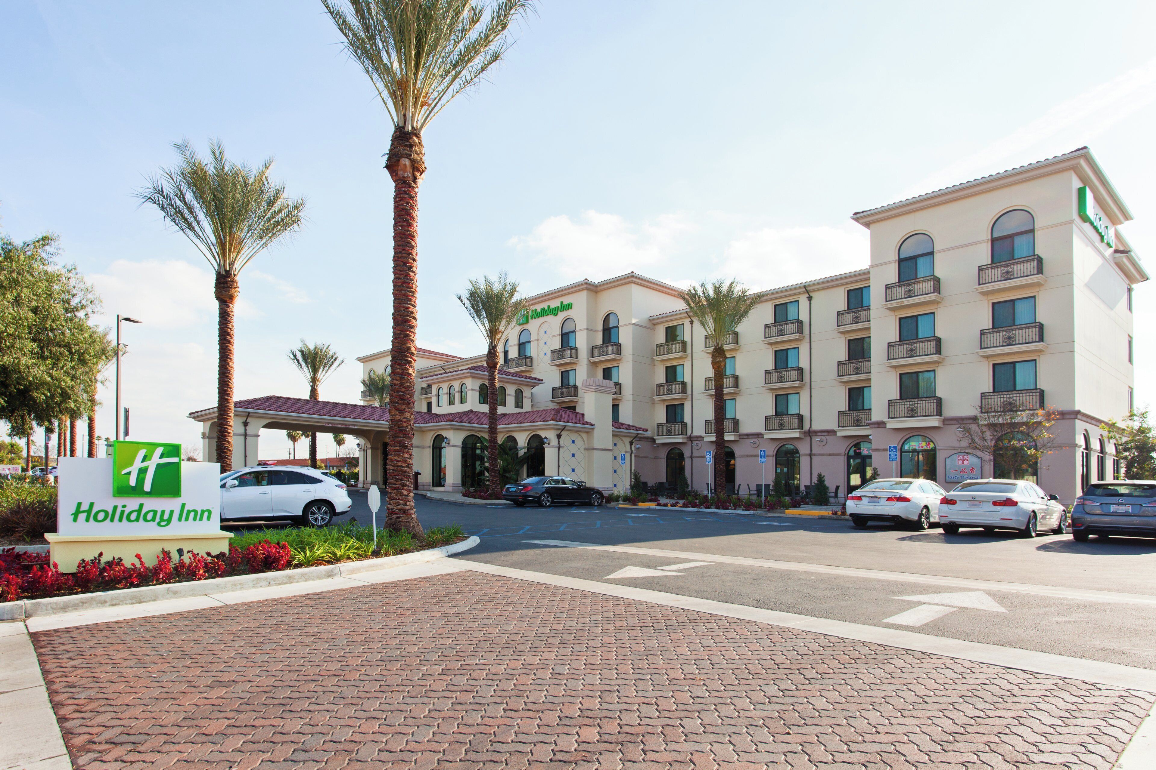 A Holiday Inn hotel with a brick-paved entrance, palm trees, and a parking lot with several cars.