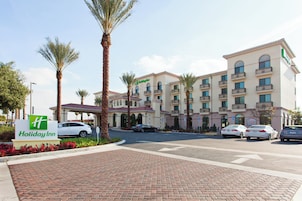 A Holiday Inn hotel with a brick-paved entrance, palm trees, and a parking lot with several cars.