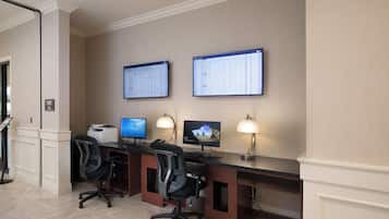 A hotel business center with two computer monitors, a printer, and two office chairs.
