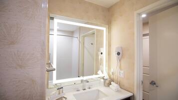 Un baño con un espejo grande, un lavabo, un perchero para toallas y un secador de pelo montado en la pared.