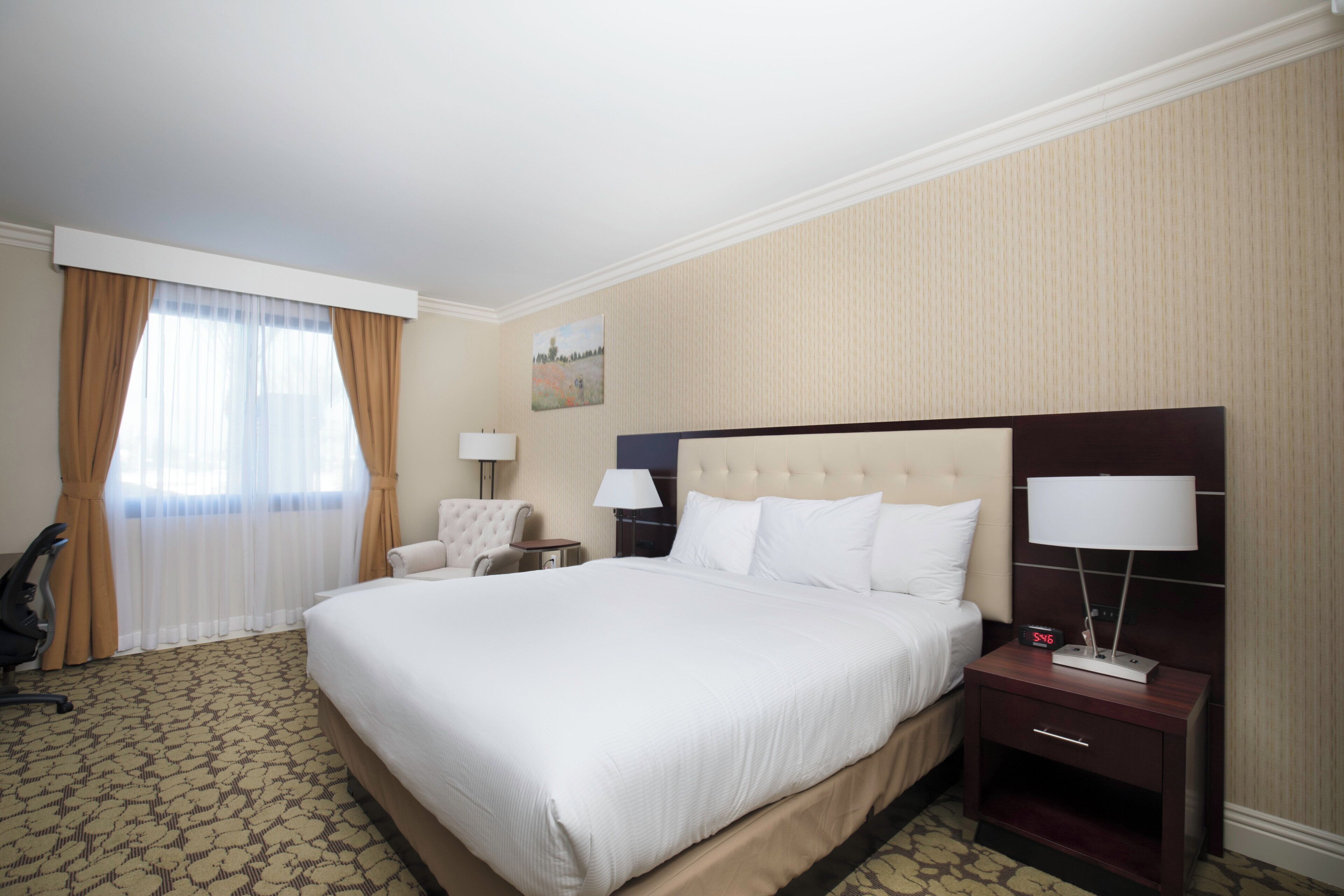Una habitación de hotel con una cama grande, dos mesitas de noche con lámparas, una silla y un cuadro en la pared.
