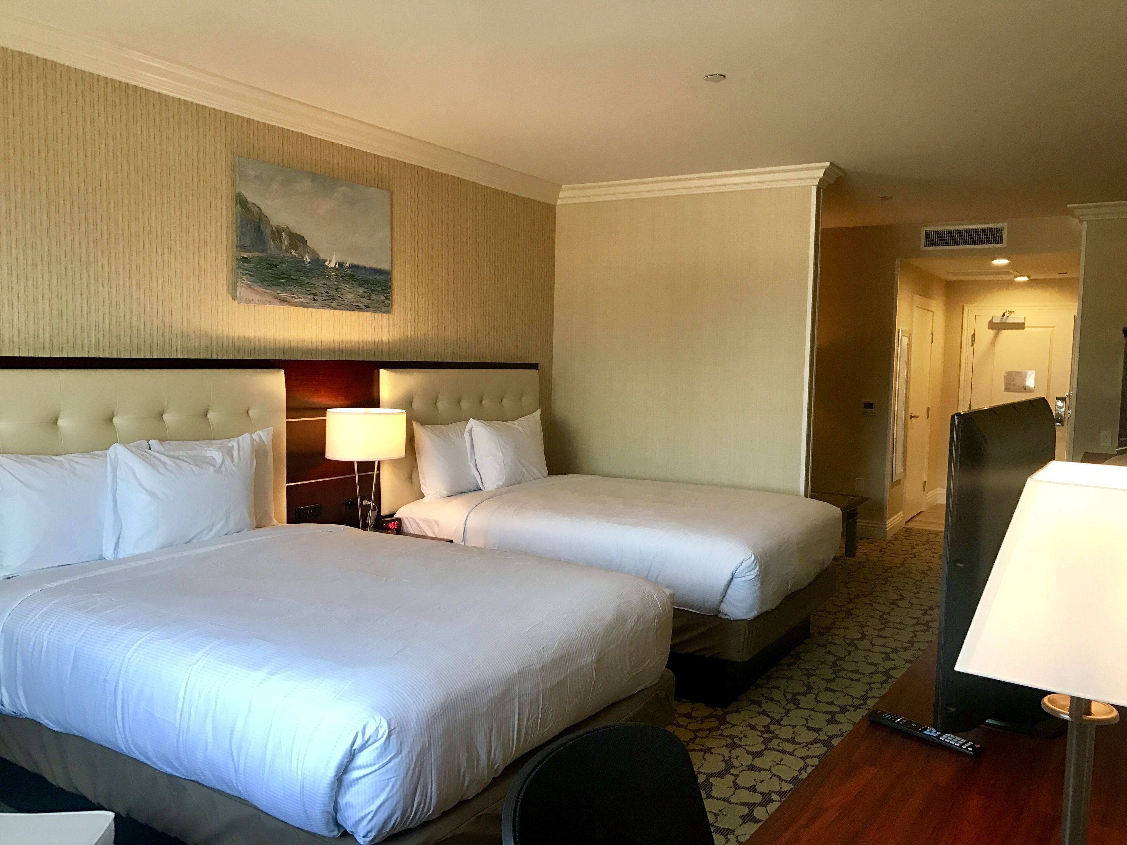 Una habitación de hotel con dos camas, un cuadro en la pared, una lámpara y un control remoto en el suelo.