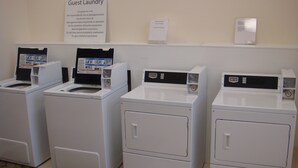 A row of white Maytag front-loading washers with control panels, a 'Guest Laundry' sign above, and a 'Washer & Dryer Free of Charge' sign to the right.