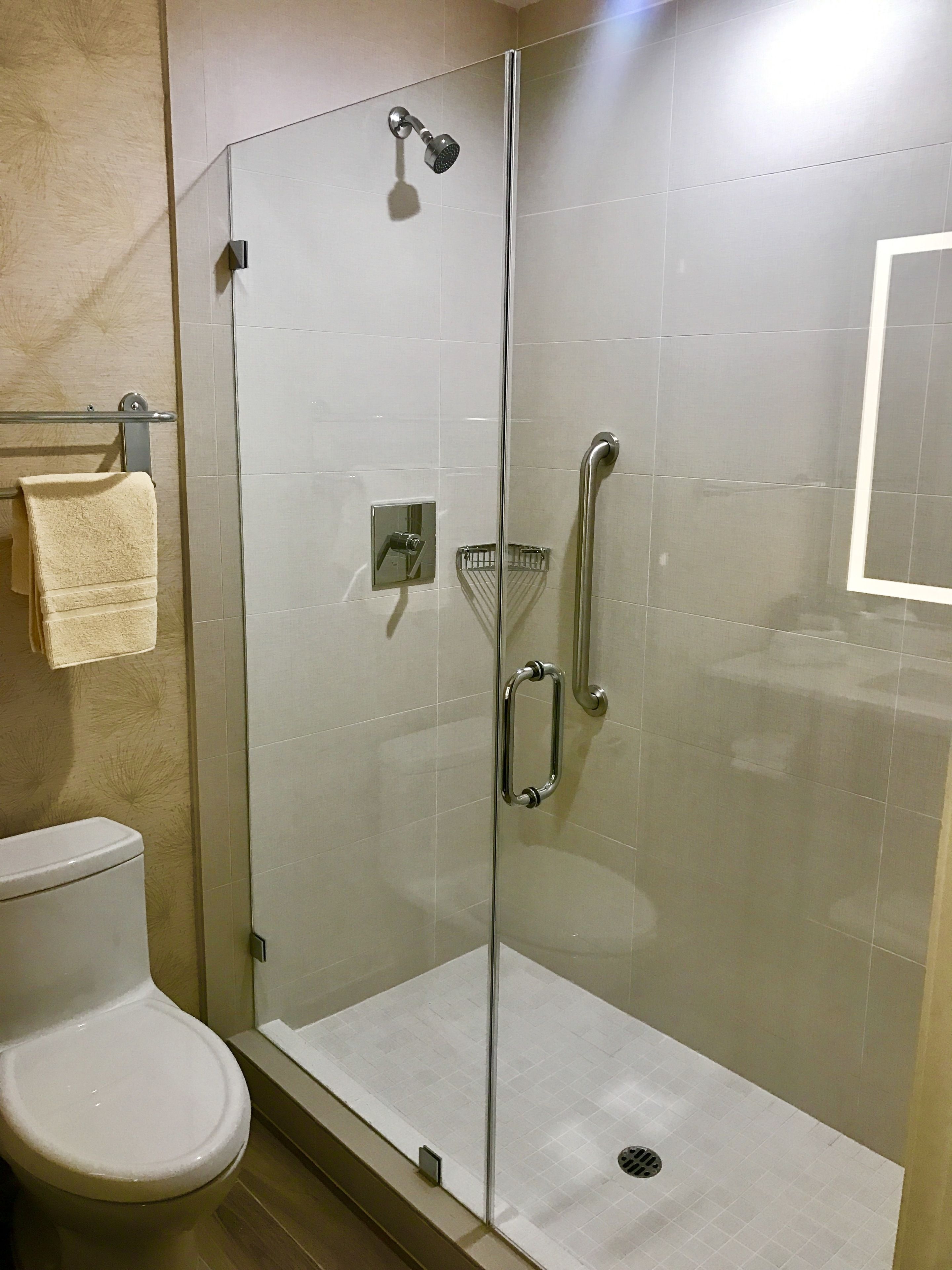 A glass-enclosed shower stall with a handheld showerhead, a glass door, and a towel rack with a folded towel.