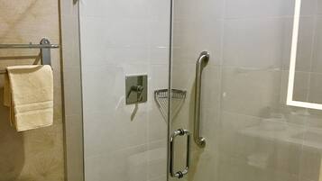 A glass-enclosed shower stall with a handheld showerhead, a glass door, and a towel rack with a folded towel.