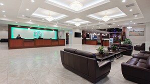 A hotel lobby with a reception desk, seating area, and a large painting on the wall.