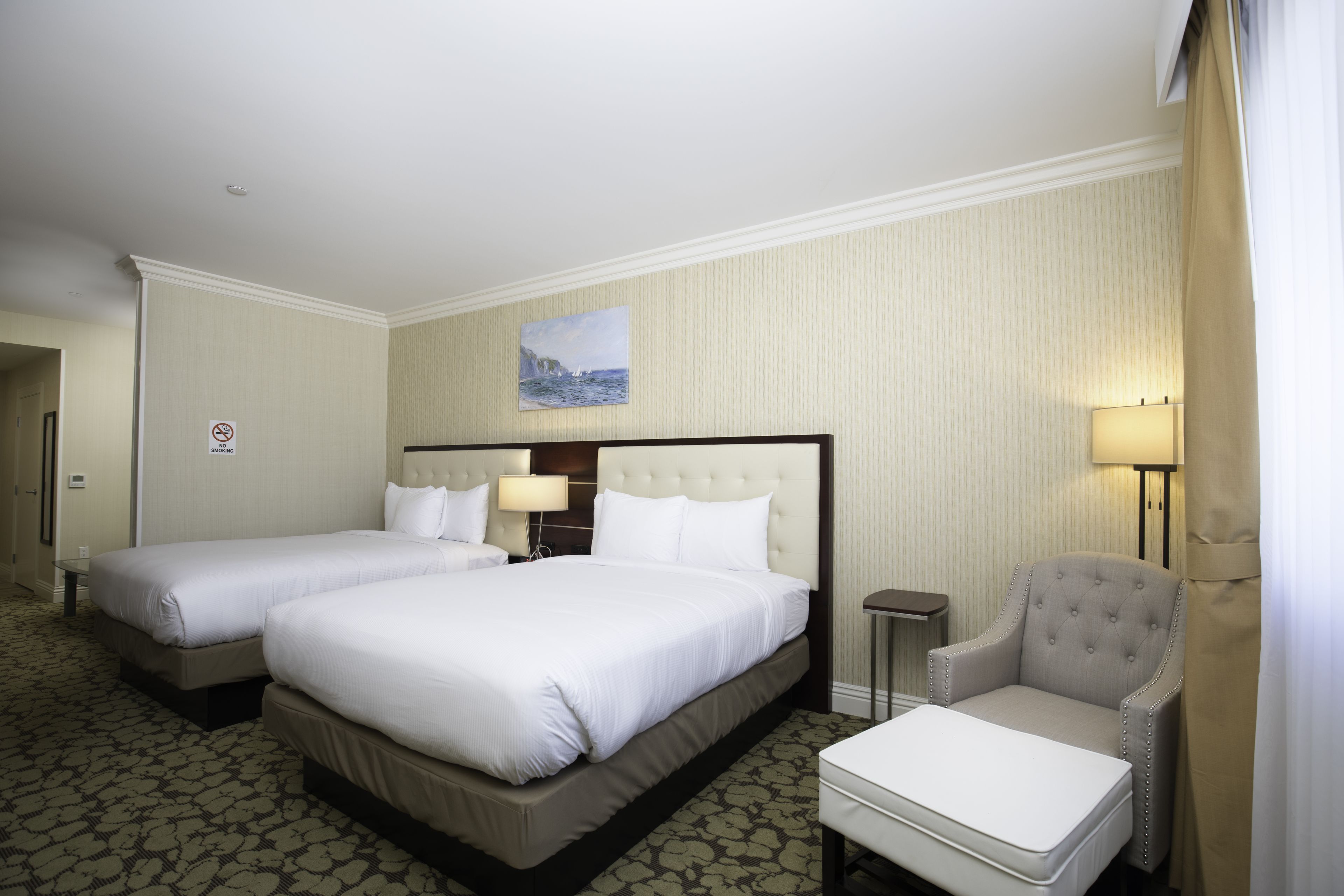 Une chambre d’hôtel avec deux lits, une chaise, une petite table et un tableau au mur.