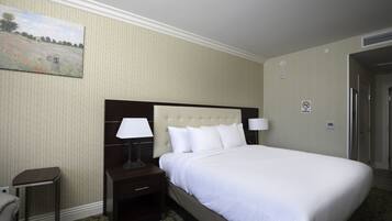 A hotel room with a large bed, two bedside tables with lamps, a painting on the wall, and a door to the right.