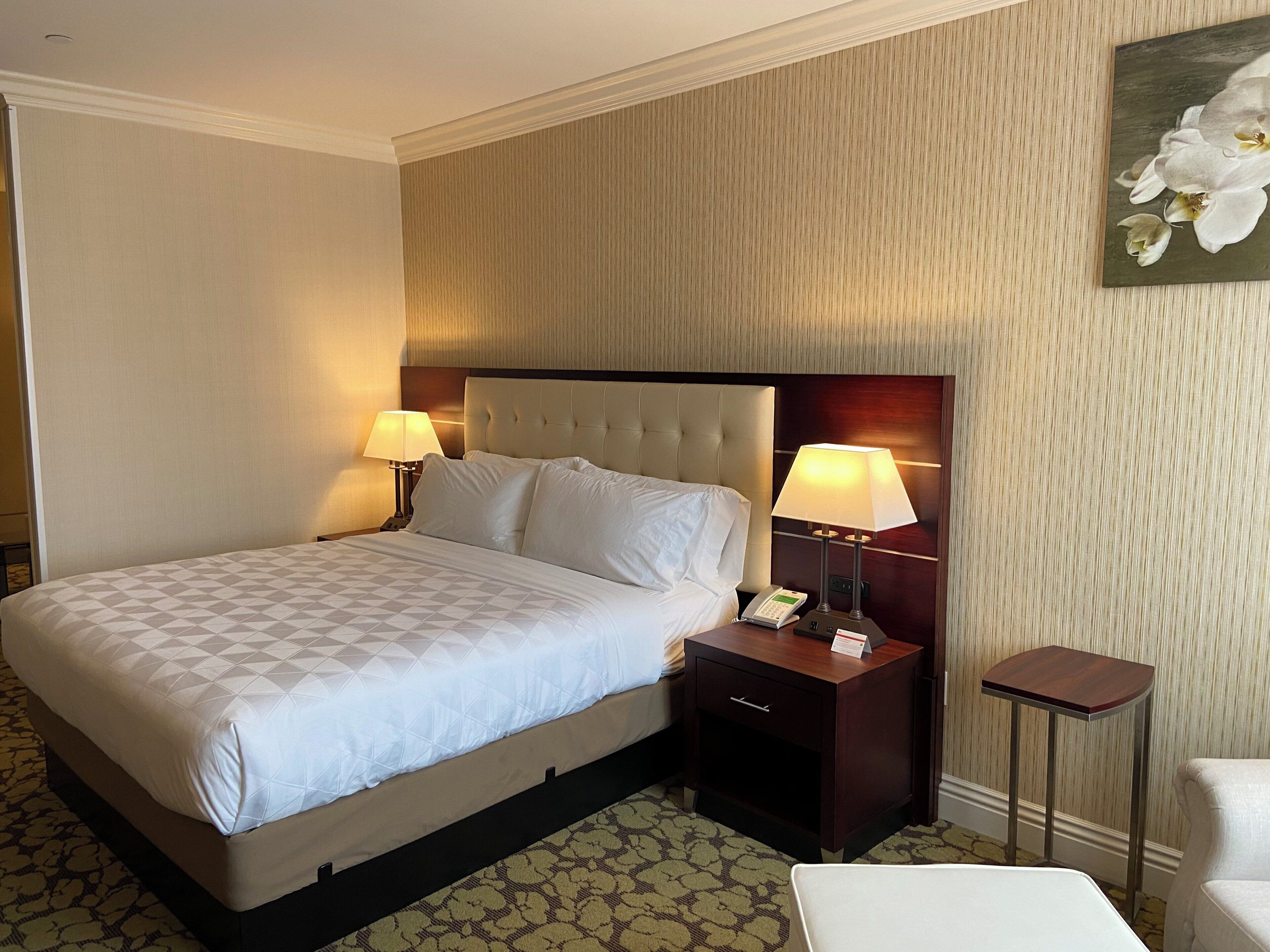 A hotel room with a large bed, two bedside tables with lamps, a small table, and a chair.