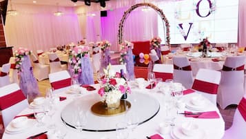 A banquet hall with round tables, white tablecloths, and floral centerpieces.