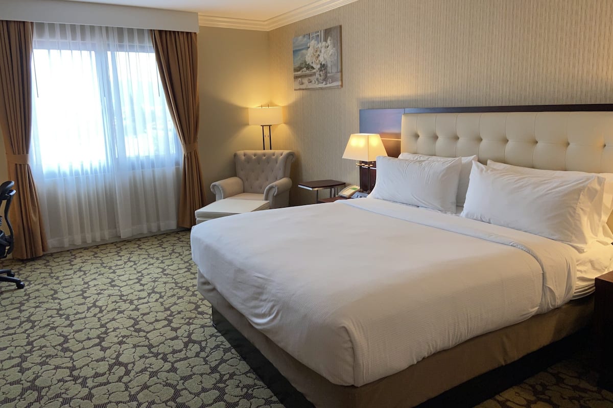 Un cuarto de hotel con una cama grande, una silla, un escritorio con una lámpara y un cuadro en la pared.