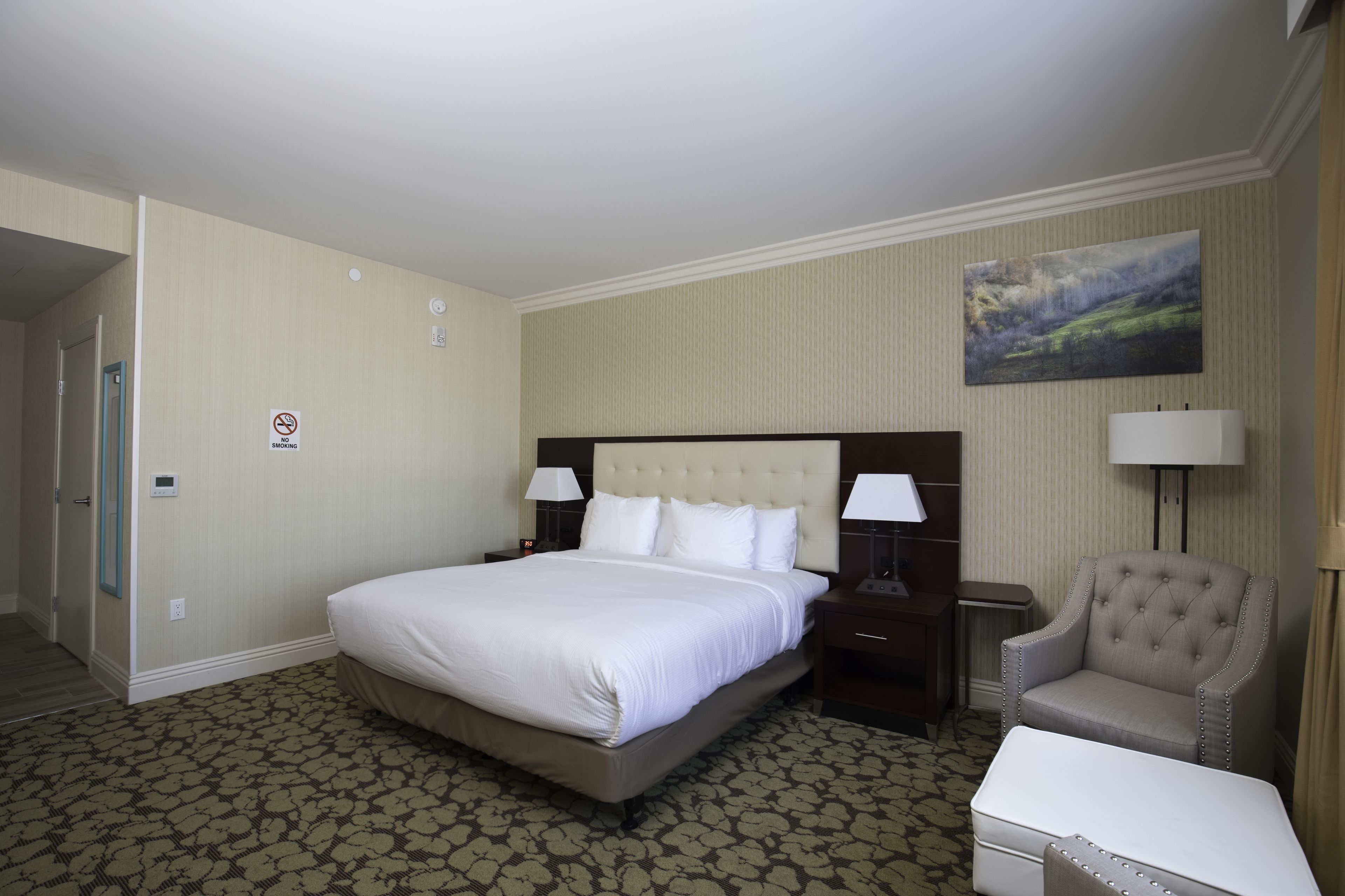 Una habitación de hotel con una cama grande, dos mesitas de noche con lámparas, una silla y una pequeña mesa.