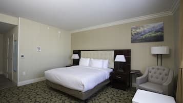 Una habitación de hotel con una cama grande, dos mesitas de noche con lámparas, una silla y una pequeña mesa.