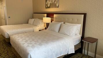 A hotel room with two beds, a nightstand with a lamp, a small table, and a wall-mounted artwork.