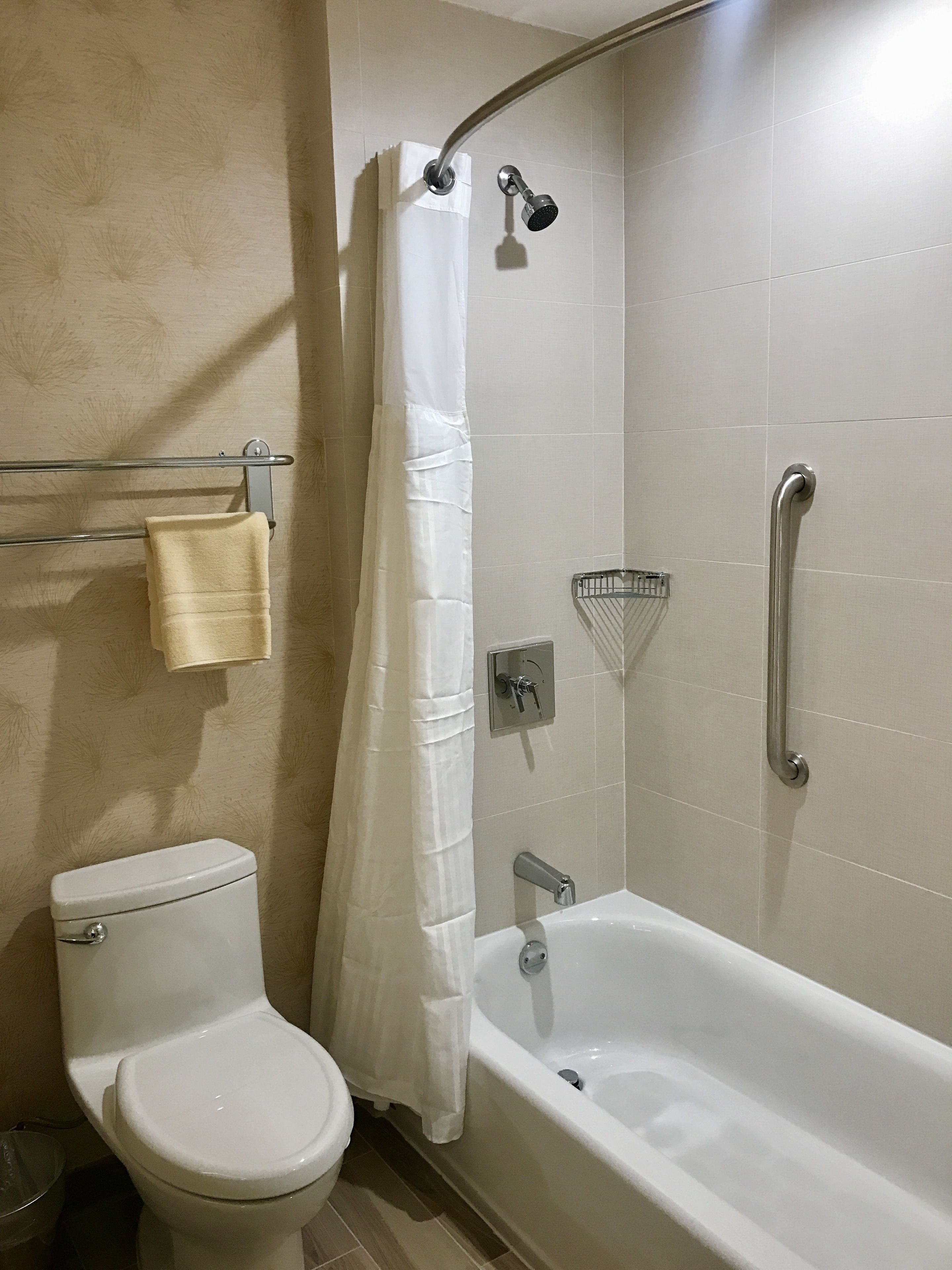 A bathroom with a toilet, bathtub, shower, and towel rack.