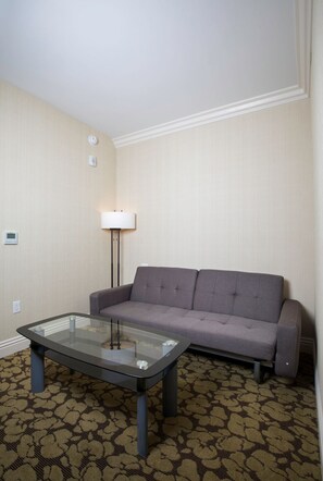 A room with a grey sofa, a glass coffee table, a floor lamp, and patterned carpet.