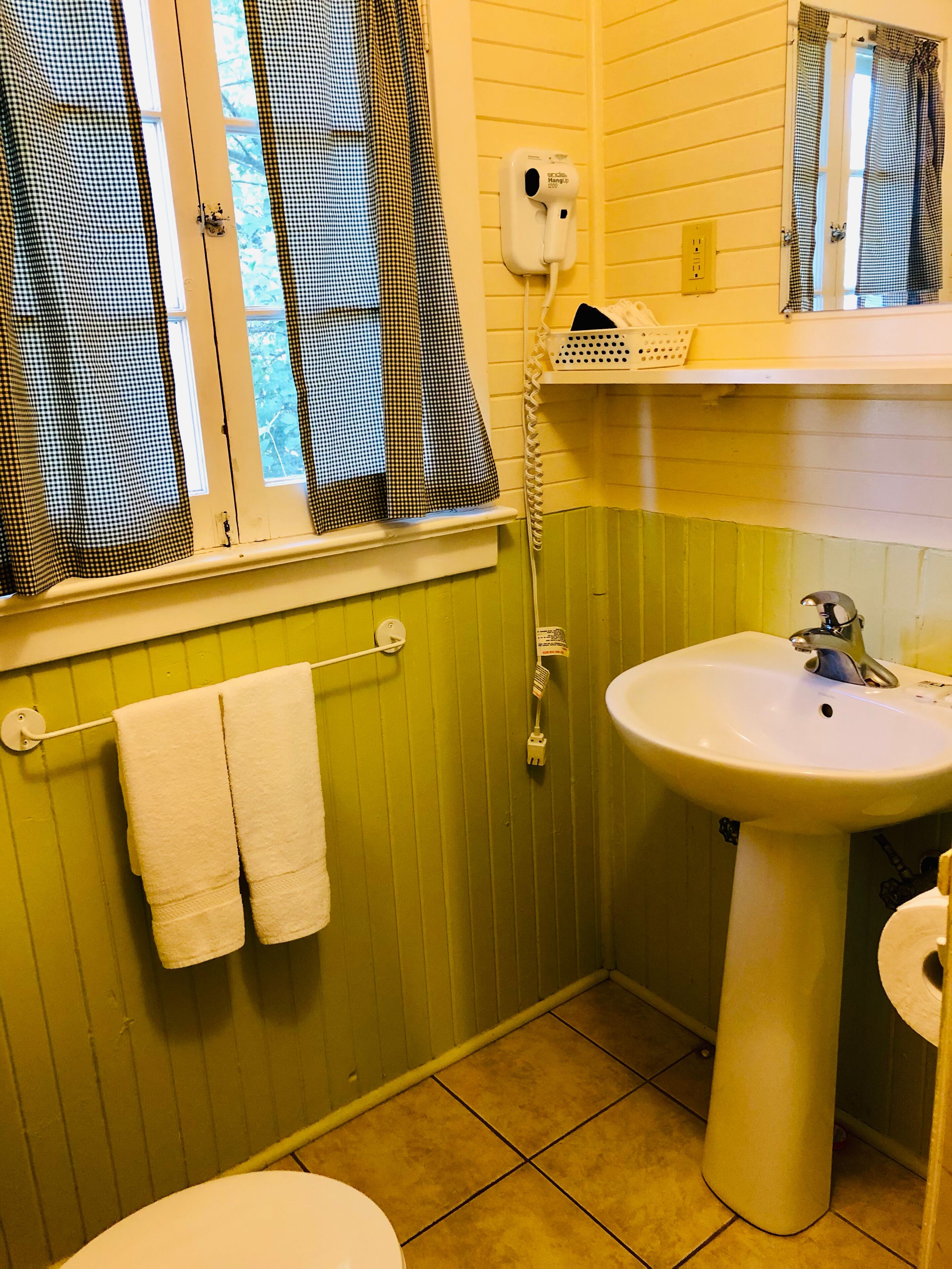 Un baño con una pared verde, un lavabo blanco y una ventana con cortinas cuadriculadas.