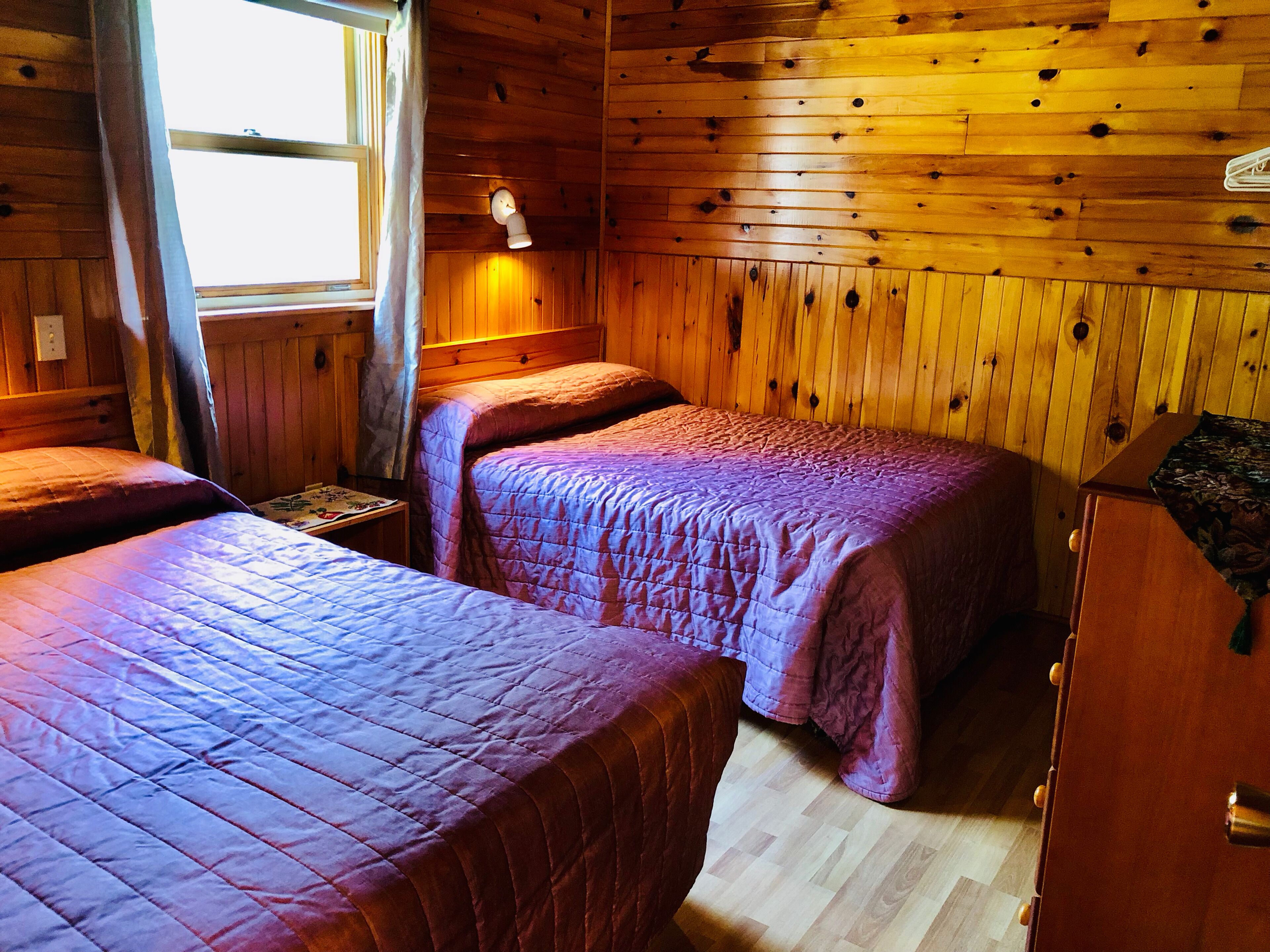 A cabin with two beds, wooden walls, a window, and a clock.