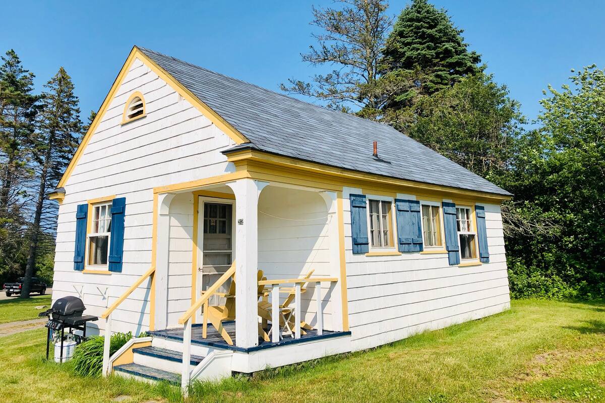 A white building with blue shutters, a porch, and a chimney.