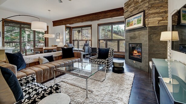 A modern living room with a stone fireplace, large windows, and a ceiling fan. - Osprey 303 (Avon)