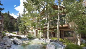 A resort with a natural pool surrounded by large rocks and trees, featuring multiple-story buildings with balconies. - Osprey 303 (Avon)