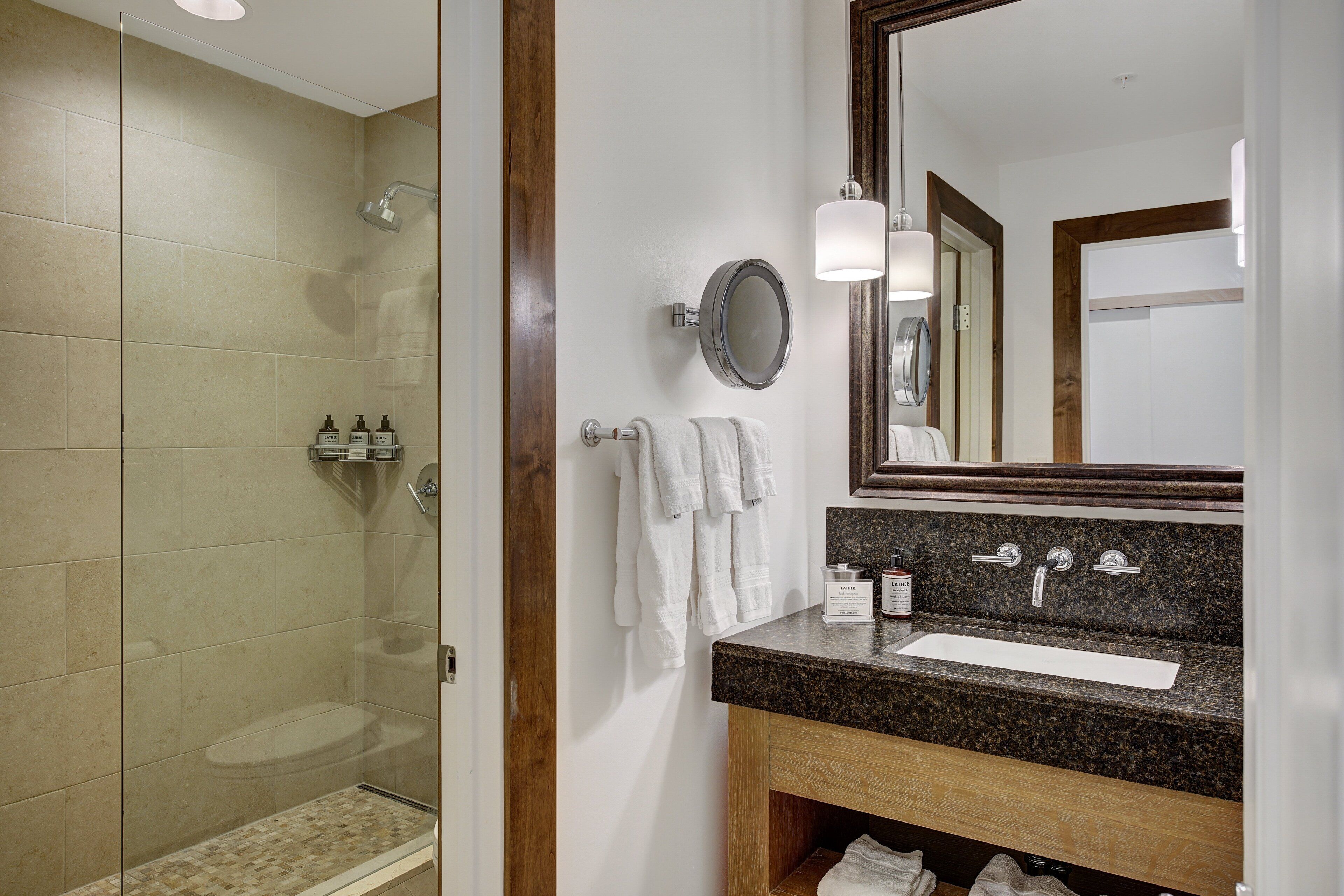 Une salle de bain moderne avec une douche à parois de verre, un lavabo doté d’un plan de travail en granit et un grand miroir.