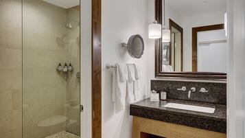 Une salle de bain moderne avec une douche à parois de verre, un lavabo doté d’un plan de travail en granit et un grand miroir.