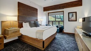 A modern bedroom with a large bed, wooden headboard, a ceiling fan, a TV, and a window with a view of trees. - Osprey 303 (Avon)