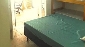 A room with a bunk bed and a single bed, a tiled floor, and a door leading to an outdoor area with a chair and a table. - Hostel Brazil Backpackers (Guarujá)