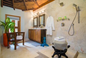 Une salle de bain avec un meuble-lavabo en bois, un grand miroir, une douche et un coin salon équipé d’un panier à serviettes.