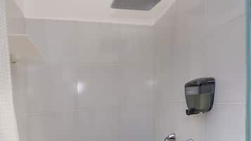 A bathroom with white tiles, a showerhead, and a soap dispenser.
