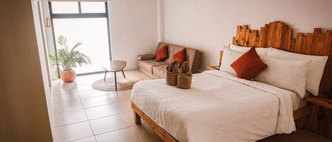 A bedroom with a wooden bed, a sofa, a small table, and a potted plant.