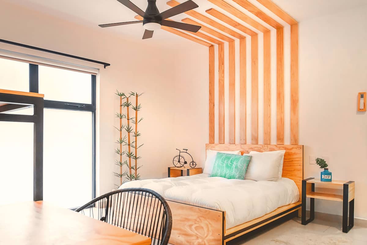 Une chambre à coucher comprenant un lit, un bureau, une chaise, un ventilateur de plafond et une fenêtre.