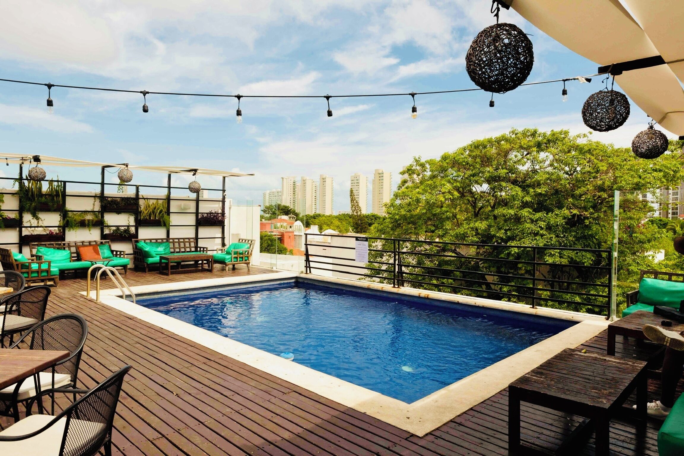 Un espace piscine sur le toit, doté d’une terrasse en bois, de chaises longues vertes et de guirlandes lumineuses décoratives.