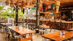 A restaurant with wooden tables and chairs, hanging decorations, and a bar area. - Nomads Hotel & Rooftop pool (Cancun)