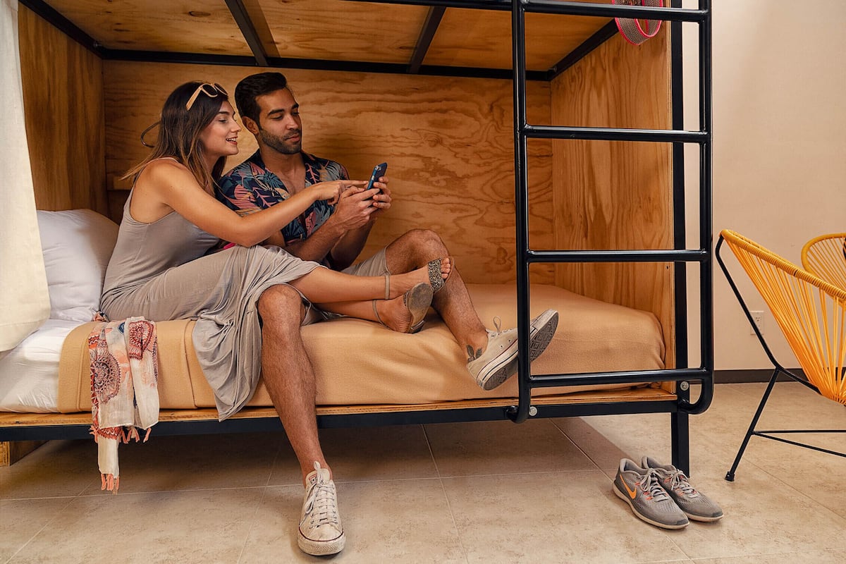Un lit superposé avec une structure en bois, un lit simple avec un matelas beige et une chaise jaune.