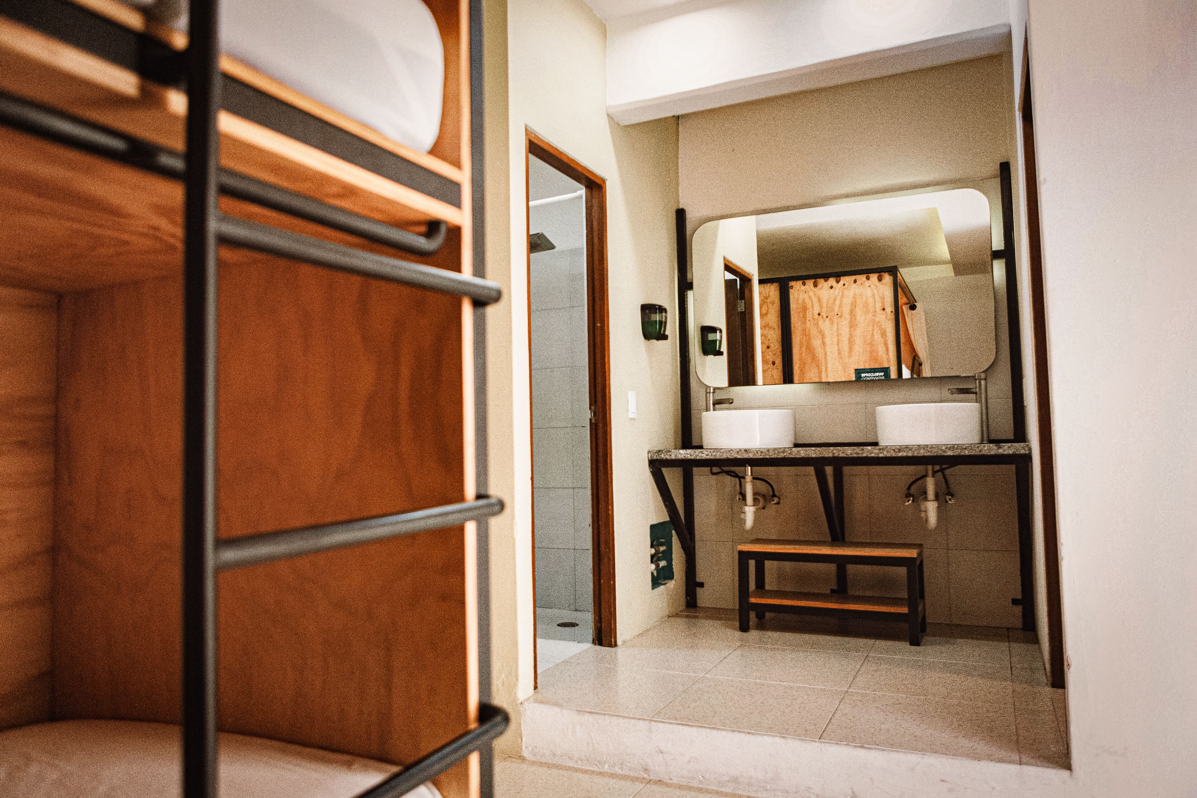 A bunk bed room with a small bathroom containing a sink, mirror, and toilet.