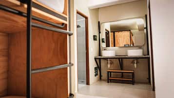 A bunk bed room with a small bathroom containing a sink, mirror, and toilet.